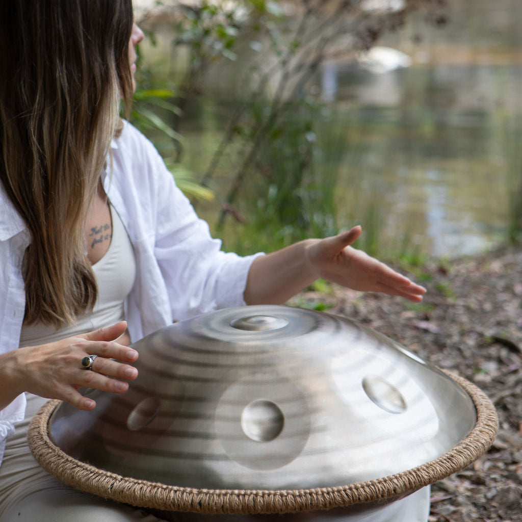 Person playing a handpan by a pond