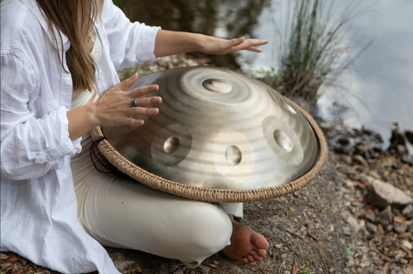 Person playing a handpan by a body of water