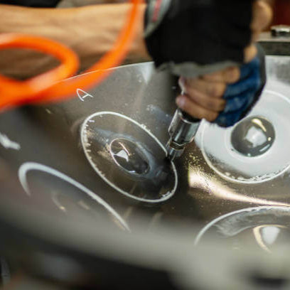 Person using a tool on a metallic surface with a blurred background